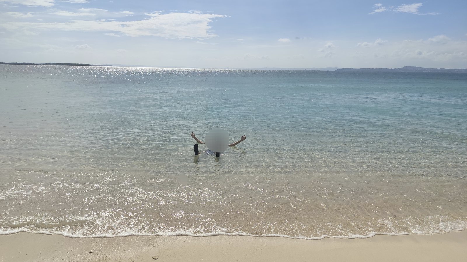 沖縄の無人島の砂浜と、遠浅の海に立って両手を広げている人